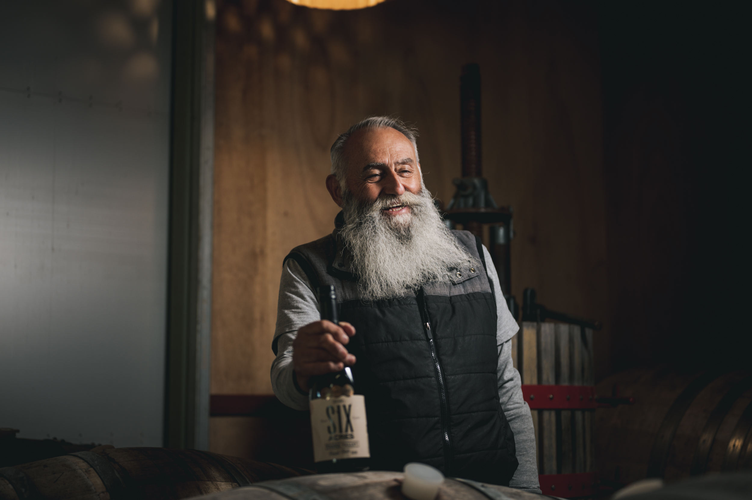 Bearded man holding wine bottle on top of barrel 